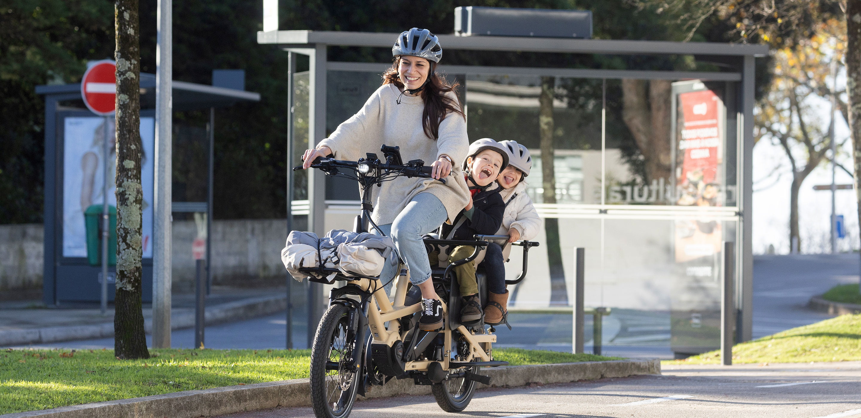 A mom riding Tern GSD cargo bike with 2 kids on the back.