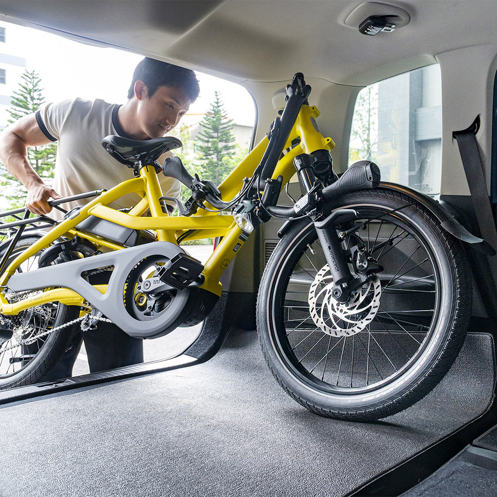 A man loading a flat-folded Tern HSD cargo e-bike into a car trunk